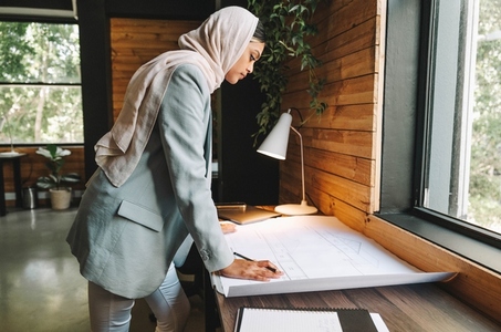 Pensive Muslim architect working with blueprints in an office