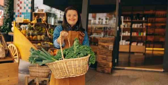 Shop employee with Down syndrome holding a basket of fresh organic vegetables
