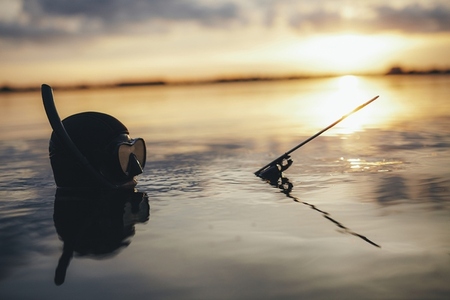 Spearfishing diver submerged in sea water at sunset