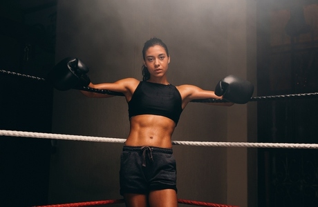 Muscular female athlete leaning against boxing ring ropes