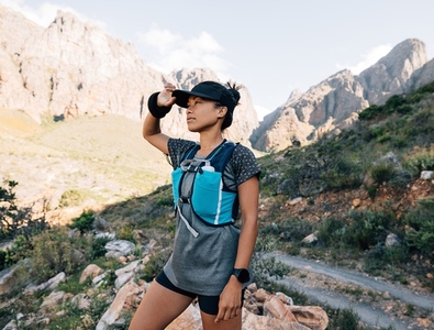 Female hiker standing in valley between mountains holding cap looking away