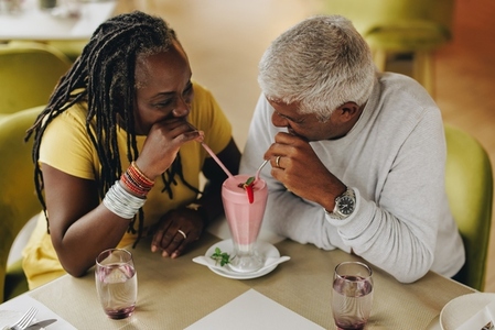 Mature couple sharing a milkshake in a cafe