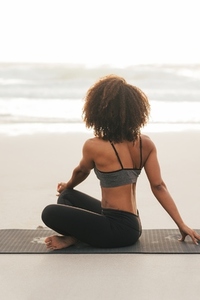 Back view of a woman sitting on yoga pose looking at the ocean  Young female meditating on beach