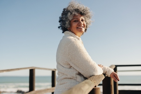 Happy senior woman smiling at the camera on a seaside foot bridge