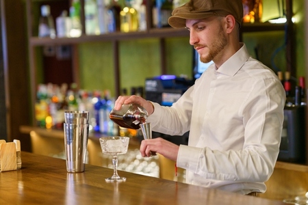 Male barkeeper pouring alcohol into shaker