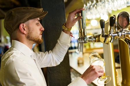 Male bartender pouring beer in beautiful pub