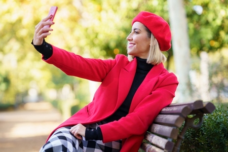 Cheerful woman taking selfie in park with red clothes