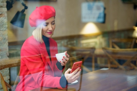 Through glass of woman with coffee browsing smartphone