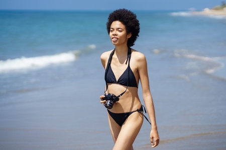 Black woman in swimsuit with photo camera at seaside