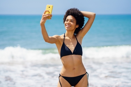 Joyful black woman taking selfie on smartphone near sea