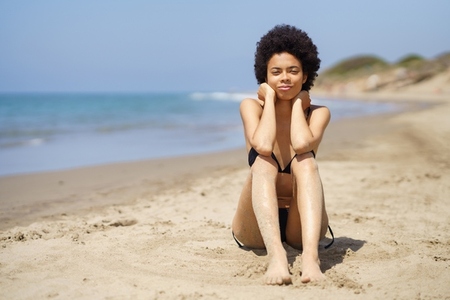 Black woman sitting on sandy beach in summer
