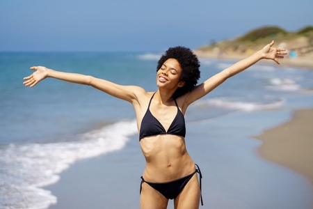 Cheerful black woman in bikini on wet seashore