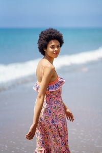 Young black woman in colorful dress on sandy seashore