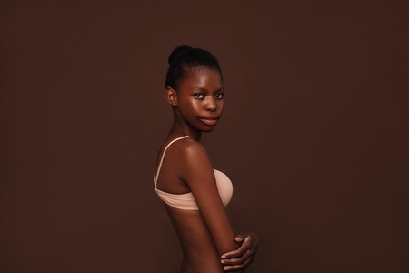 Side view of an African American girl in lingerie looking at camera against brown background