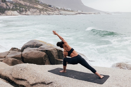 Woman practicing yoga at evening on a cliff against an ocean
