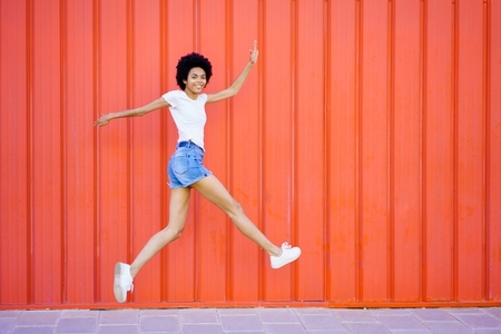 Content black woman jumping near red wall