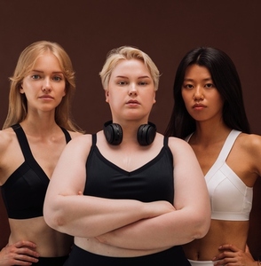 Three women with different body types standing together against brown background