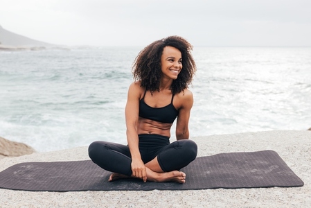 Smiling woman looking away while sitting on yoga mat by ocean  F