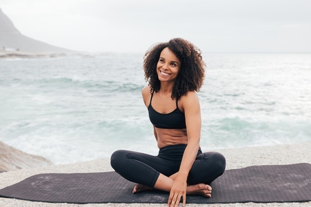 Portrait of young smiling female in sportswear sitting on yoga m