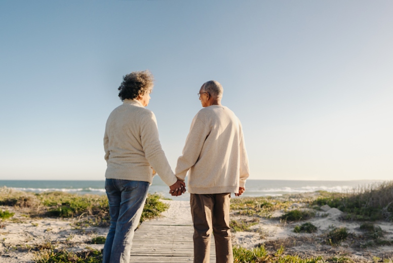 Panoramic view of a senior couple holding hands at the beach