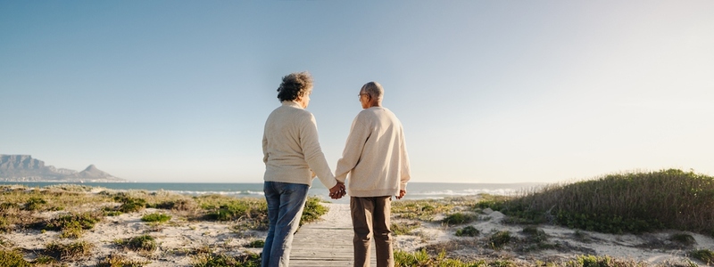 Panoramic view of a senior couple holding hands at the beach