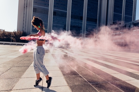 Woman with smoke grenade outdoors in city