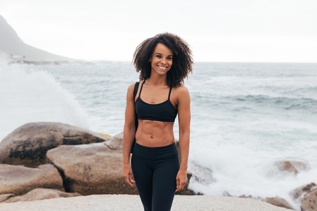 Smiling female relaxing after yoga  Muscular woman standing on rocks by ocean