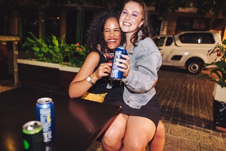 Girlfriends holding beer cans at an outdoor restaurant