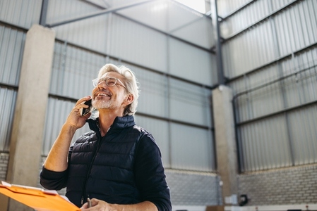Happy senior man taking a phone call in a warehouse