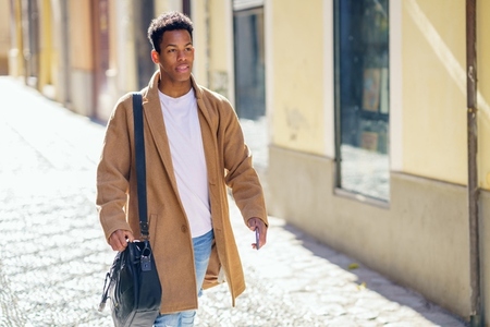 Young black man walking down the street carrying a briefcase and a smartphone