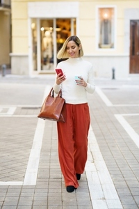 Smiling woman with takeaway coffee and bag browsing smartphone