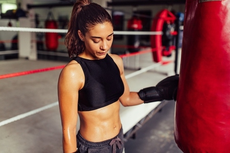 Sweaty female boxer standing next to a punching bag at the gym