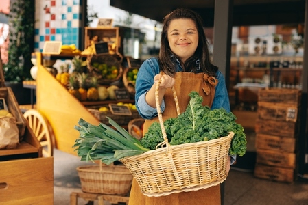 Supermarket employee with Down syndrome holding a basket of fresh organic vegetables