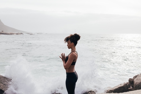 Cropped shot of young woman with folded hands meditating by ocean with closed eyes