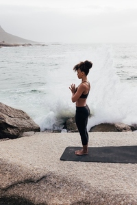 Full length of slim woman meditating against the waves  Side view of young female practicing yoga outdoor by ocean