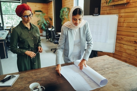 Two Muslim architects working with blueprints in a modern office