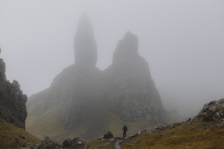Man hiking below foggy Old Man of Storr rock formation