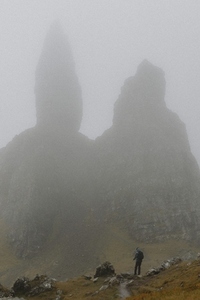 Hiker standing below foggy Old Man of Storr rock formation