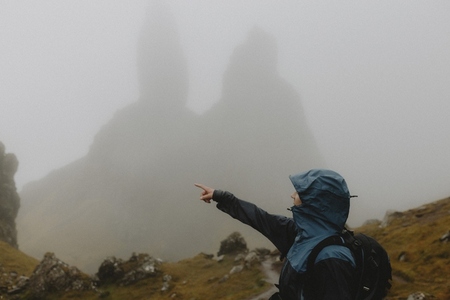 Man in ran jacket hiking below foggy Old Man of Storr rock formation