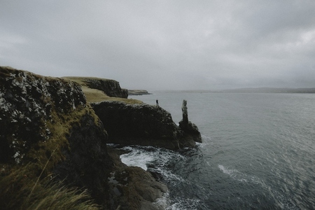 Hiker in distance at edge of cliff overlooking ocean