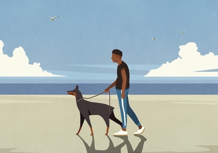 Man walking Doberman Pinscher on leash on sunny ocean beach