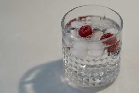 Gin and tonic in double old fashioned glass with ice and raspberries