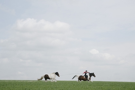 Girl horseback riding pulling horse on lead in open field