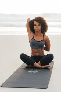 Woman sitting on mat at beach practicing Gomukhasana pose