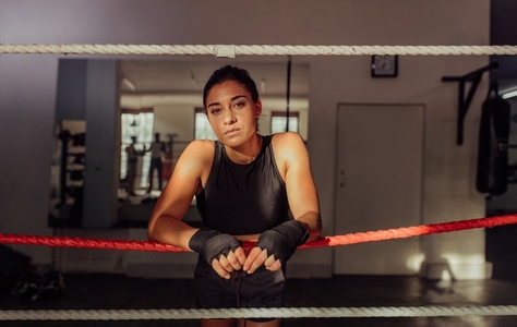 Confident female boxer leaning on boxing ring ropes