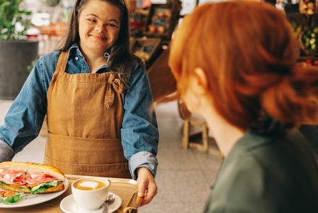 Cheerful waitress with Down syndrome serving a customer in a cafe