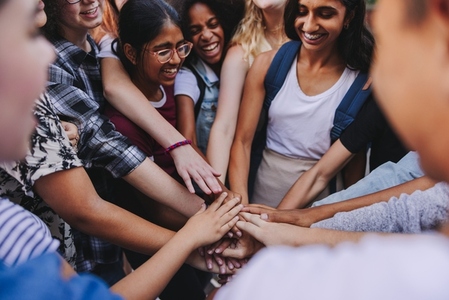 Group of happy teenagers putting their hands together in a huddle
