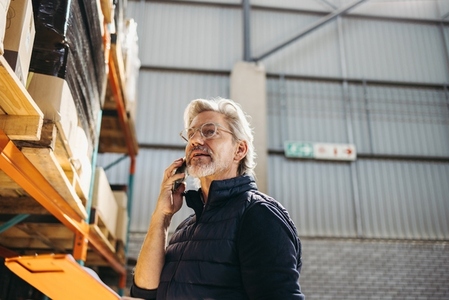 Senior man taking a phone call in a distribution warehouse
