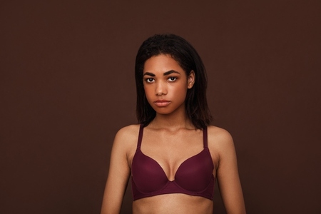 Portrait of a young woman with black hair against brown background  Young slim female in lingerie looking at camera in studio