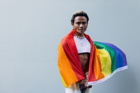 Portrait of a young guy with lgbt flag posing outdoors at grey wall